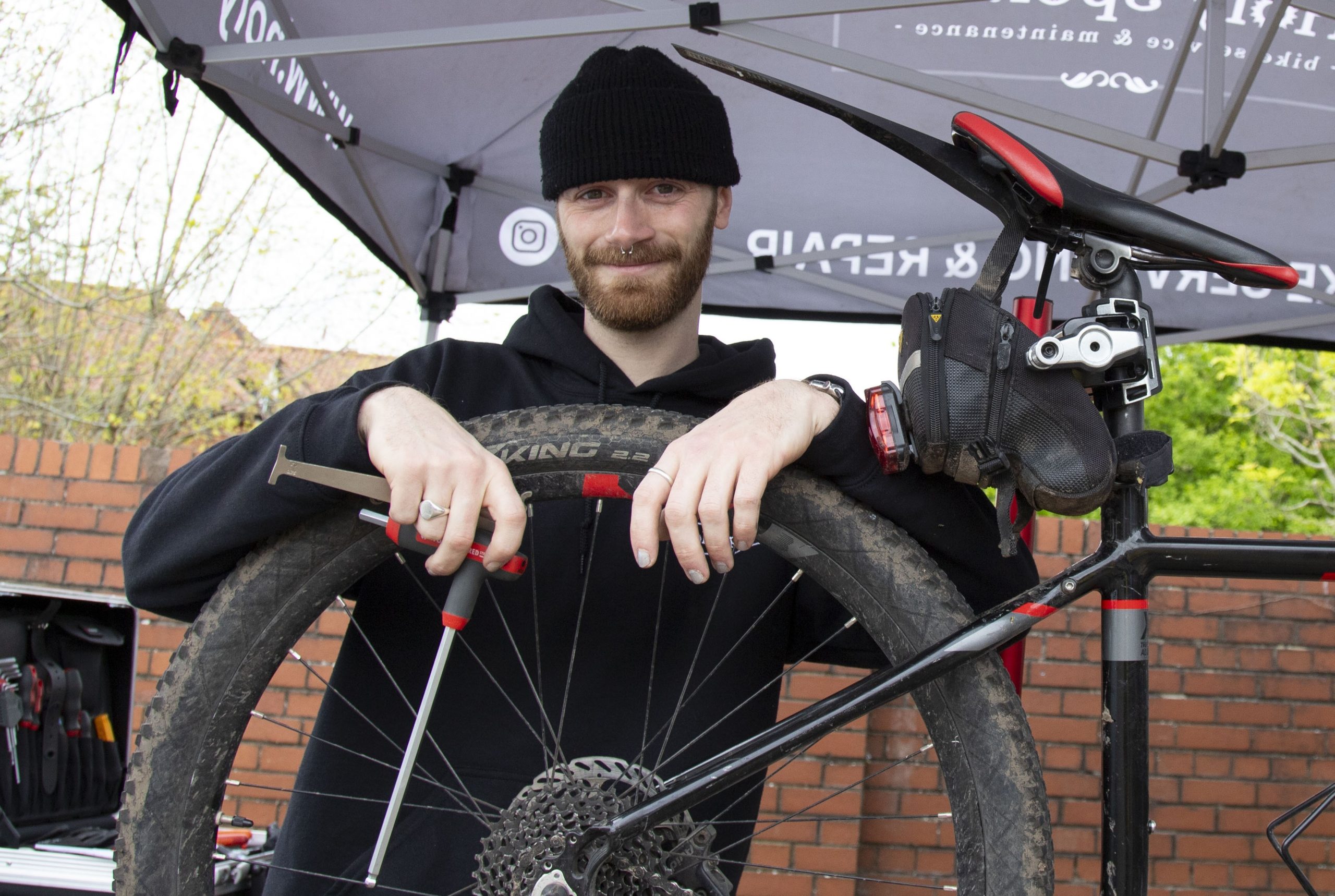 Man poses with bike holding a tool to repair it.