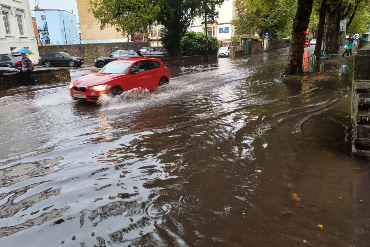 A car travelling through a flood on Whiteladies Road.